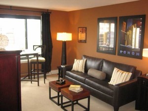 Phòng khách ấm với tường nâu, sofa da tối màu và hai khung tranh