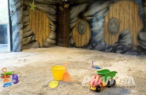 Khu vui chơi trong nhà với sàn cát nhân tạo và đồ chơi xẻng, xô, xe tải